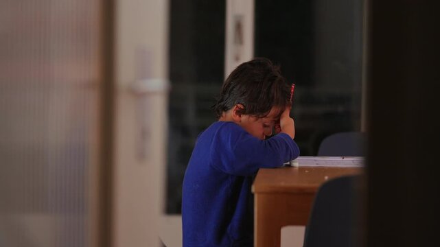 Focused young boy stands at the home table while writing in an educational workbook, demonstrating concentration, persistence and self directed homeschool learning