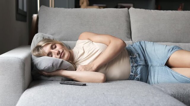 Smiling young transgender woman in casual wear sleeping by remote control on sofa in living room at home