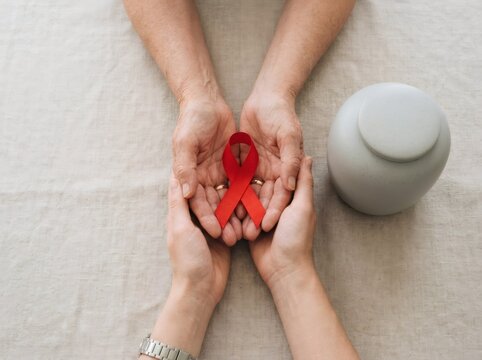Hands holding a red awareness ribbon with wedding rings. Support, commitment, remembrance, and solidarity concept for health campaign and charitable cause.