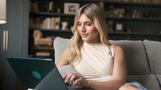 Happy young transgender freelancer woman smiling as she works on laptop while sitting on sofa in living room at home