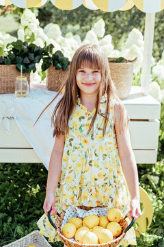 Smiling young girl Holding wicker basket filled with fresh lemons outdoors in a bright summer garden setting.