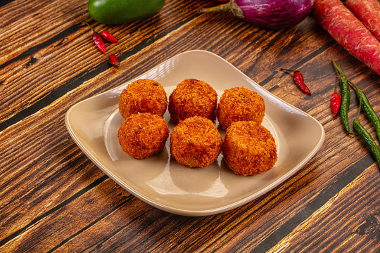 Crispy fried croquettes on ceramic plate with fresh vegetables on rustic wood