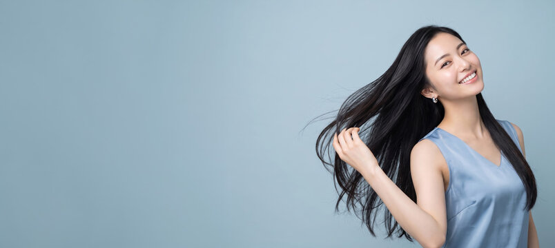 風になびく黒髪を手で触り微笑むノースリーブ姿の女性