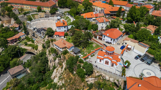 Aerial view of the Ancient Theatre of Philippopolis surrounded by historic buildings, red-tiled roofs, and lush greenery in Plovdiv, Bulgaria.