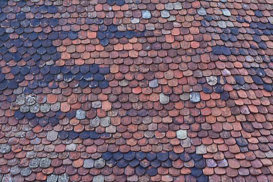 Old Weathered Clay Roof Tiles Pattern with Mixed Red and Dark Grey Tones on a Historic Building