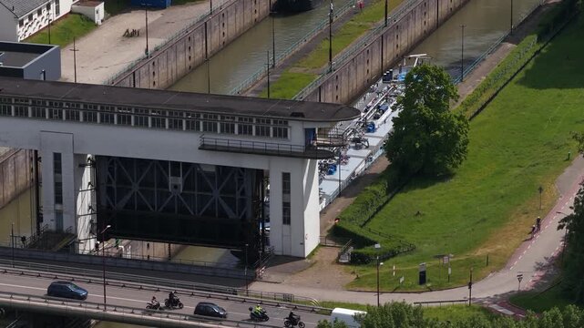 Aerial view of boat moving through industrial canal lock system with motorcycles driving on bridge road nearby.