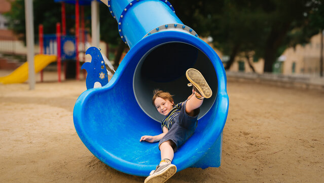 Happy boy sliding out of a blue tube slide at playground