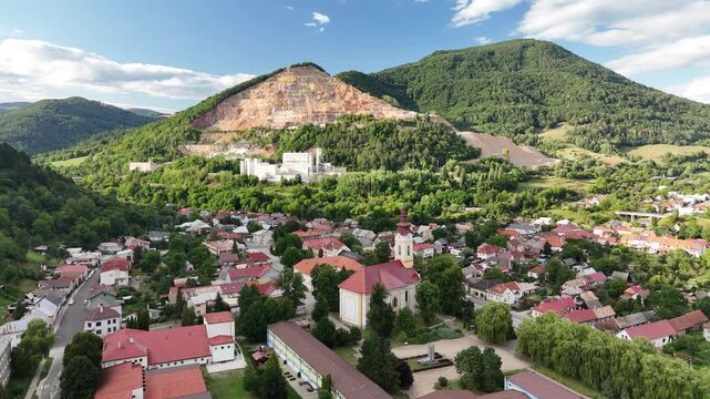 Aerial view of Tisovec town featuring the historic church, residential rooftops, and the industrial quarry set against the green hills of Tisovec, Banska Bystrica Regio, Slovakia.