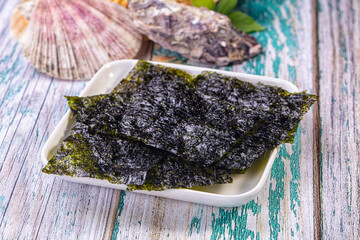Crispy nori seaweed sheets on white dish with seashell and fish on rustic wooden background © Andrei Starostin