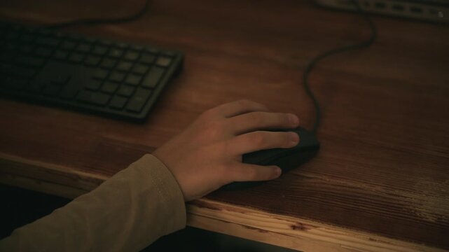 Young person operating a computer mouse while sitting at a desk and playing video game. Internet use, gaming, education and modern technology theme. 4K.