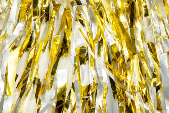 Festive background featuring shiny gold metallic foil tinsel streamers. Holiday or celebration background