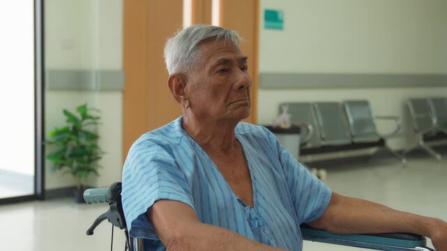An elderly male patient sitting in a wheelchair and looking thoughtful in a hospital hallway
