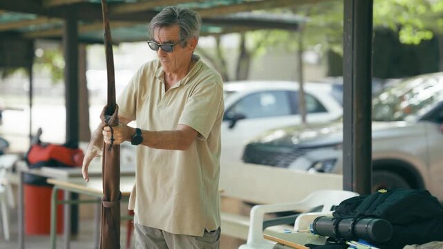 Senior man with sunglasses taking his recurve bow out of its case. Professional archer getting ready for training at an outdoor range