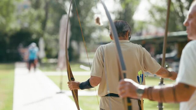 Senior man concentrating while aiming and shooting an arrow with a traditional longbow. An archer enjoying his outdoor sport and hobby