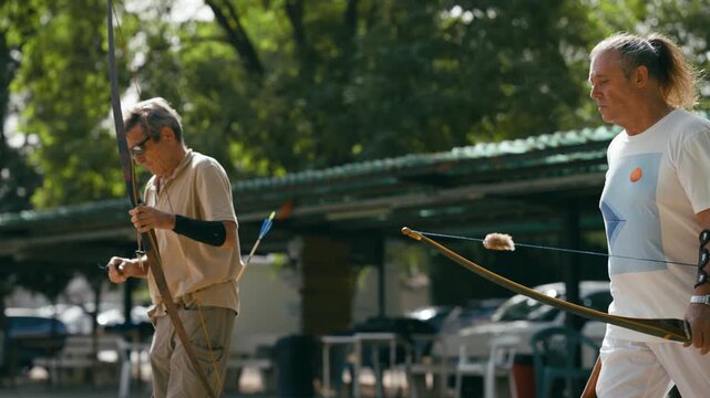 Two experienced senior archers preparing their equipment and shooting arrows with traditional bows during an outdoor practice session