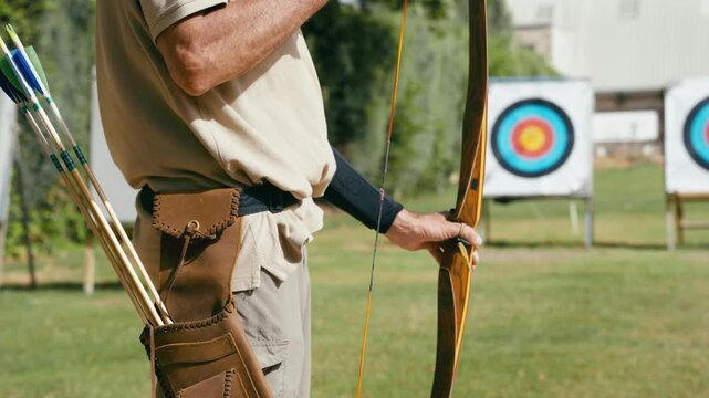 Mature man aiming and shooting a wooden bow during an archery competition. An archer trains concentration, precision, and skill outdoors