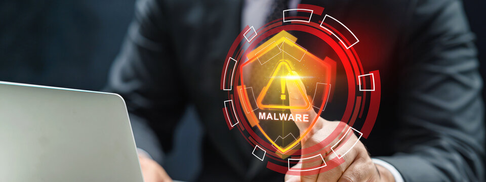 Businessman touching a virtual HUD interface showing a malware warning shield with a laptop nearby. Cybersecurity concept