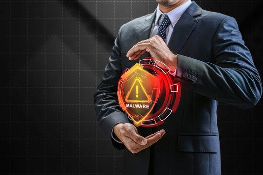 Businessman displaying a glowing orange holographic shield with a malware warning alert, representing cybersecurity threats and data defense. Cybersecurity concept