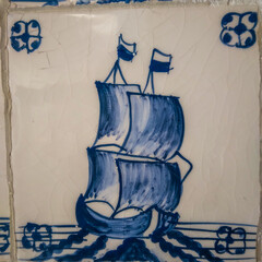 Hand painted ceramic tile depicting a classic sailing ship with blue ink sketches on a white crackled background featuring decorative floral corner patterns for interior design © Graphixa