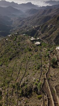 Stunning aerial footage revealing ancient agricultural terraces and traditional stone houses nestled in the rugged mountains of taiz, yemen, with a vast valley visible in the distance.