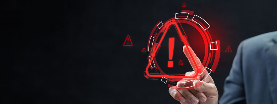 Businessman pointing at a glowing red warning triangle icon on a digital interface, symbolizing cybersecurity alert, system error, or risk management on a dark background. Cyber threat concept
