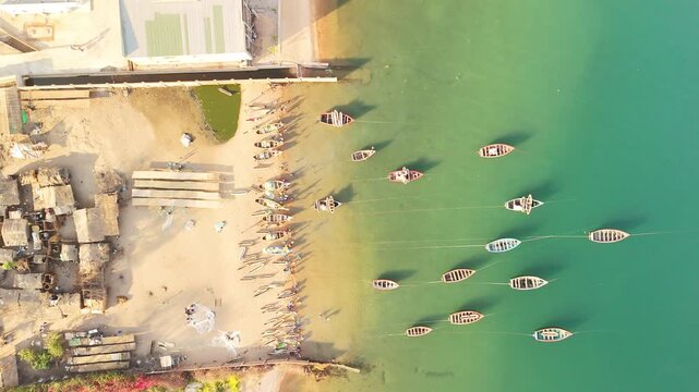 Top-down drone view of fishing canoes lining a golden sandy shore and floating in turquoise Lake Malawi beside nets and simple lakeside homes.