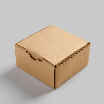 A small closed brown corrugated cardboard box on a neutral light gray background, ideal for packaging and shipping mockups. Mockup or Copyspace