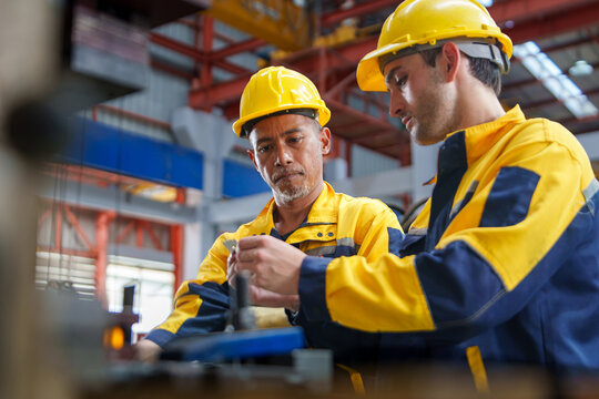 Two construction workers inspecting equipment and discussing work in a manufacturing environment for training and teamwork purposes.