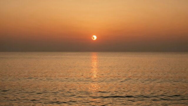 Partial solar eclipse over the ocean during a golden sunset, creating a serene and atmospheric view of the celestial event
