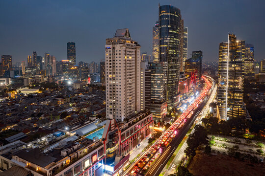 Aerial view of Jakarta skyline at dusk featuring bright highway light trails and modern skyscrapers juxtaposed against dense urban neighborhoods. Jakarta, Indonesia. Cityscapes background