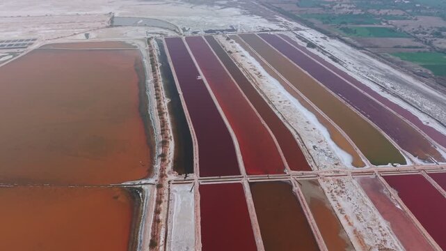 Drone footage reveals geometric salt evaporation ponds with vibrant pink, red, and brown hues at Sambhar Salt Lake. The aerial perspective captures the rectangular basins separated by white borders.