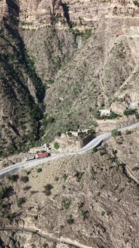 Aerial view of a winding road carved into the rugged, arid mountains of taiz, showcasing remote villages and dramatic landscapes with vehicles navigating the treacherous terrain. In taiz yemen