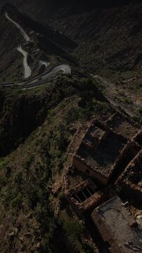 Aerial view of an ancient fortress ruin on a rugged mountain ridge overlooking a winding road and a village nestled in a lush green valley in the remote yemeni highlands of taiz. In taiz yemen