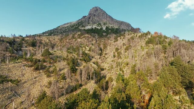 Nevado de Colima (Zapotepetl) rocky summit rising above pine covered volcanic slopes in Nevado de Colima National Park, Jalisco, Mexico. Approaching aerial view.