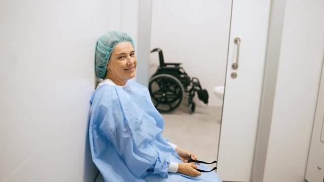 Tired but smiling female surgeon in scrubs taking a break after a difficult operation. Exhausted doctor sitting on the floor in a hospital corridor
