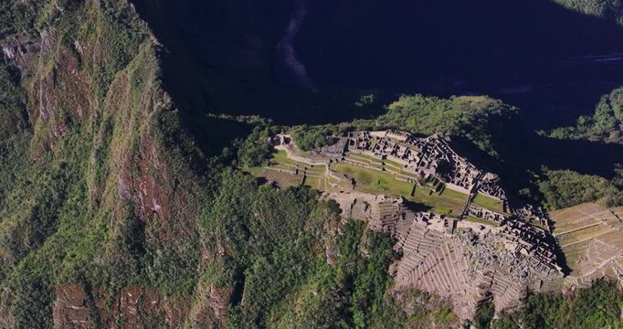 Aerial view of the ancient Incan ruins of the Historic Sanctuary of Machu Picchu nestled in the Andes mountains with green terraces and stone structures in Urubamba Province, Cusco, Peru.
