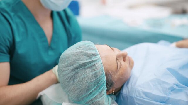 Medical team preparing an unconscious elderly woman for surgery. A doctor in scrubs comforts the patient lying on the operating table