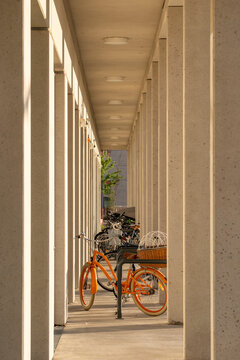 Orange bicycle parked beneath a long concrete colonnade in Vienna Austria with repeating columns and warm sunlight creating strong depth and perspective