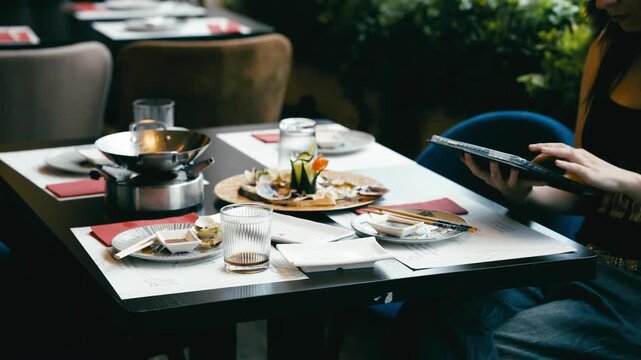 Messy table after a meal in an Asian restaurant. Woman using a digital tablet to order more food from the menu in an all you can eat buffet