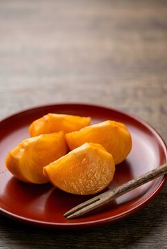 Sliced persimmon fruit on a traditional lacquerware plate with a wooden pick