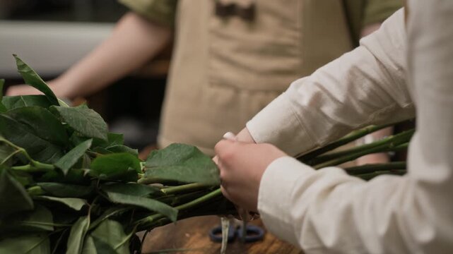 Young adult Caucasian female florists tying bunch of green rose stems with string in wholesale flower warehouse. Video is perfect for small business marketing and floristry training