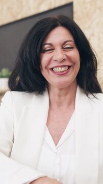 Confident senior businesswoman looking at the camera during a video call. She is speaking and smiling while working remotely from her office
