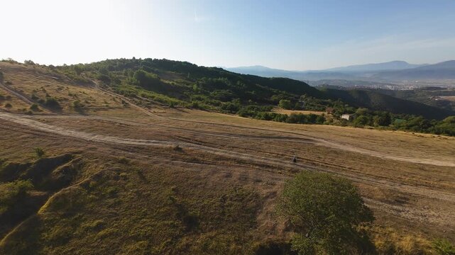 Aerial landscape drone view of rolling agricultural fields and forested foothills at golden hour