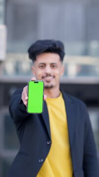 Young Moroccan businessman holding a smartphone with a green screen mockup. Man presenting a mobile device to the camera with a confident smile. Vertical