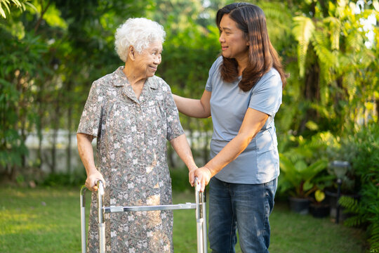 Caregiver help Asian elderly woman patient walk with walker in park.