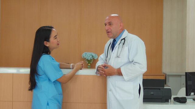 A male doctor and a female nurse chatting at the reception counter in a hospital hallway.