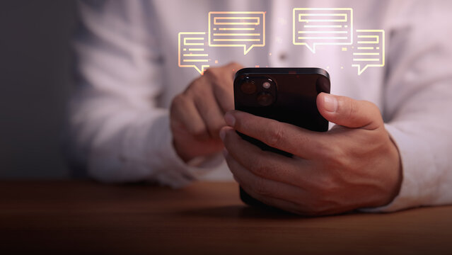 Close-up of adult man using a smartphone with glowing virtual speech bubbles. Concept of digital communication, online chat, social media networking, and modern messaging technology.