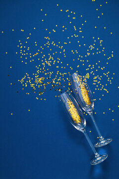 Elegant New Year flat lay banner with two champagne flutes filled with golden star confetti on deep blue background with creative dynamic negative copy space for festive holiday text.