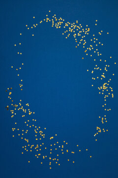 Minimalist New Year celebration vertical flat lay with golden star confetti arranged in a circle frame on a deep blue background with creative central negative copy space for holiday design.