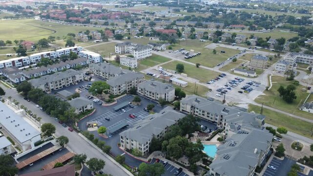 Modern residential community borders Mahncke Park in South Texas near Broadway corridor. Swimming pool courtyards flank multi story apartment blocks, asphalt parking bays, San Antonio